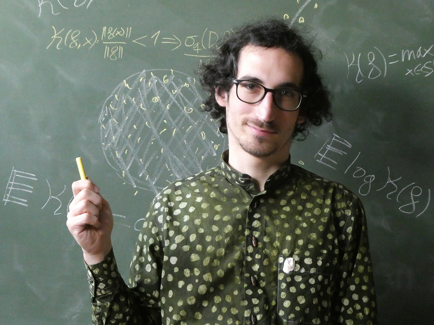 Josué Tonelli-Cueto in fron a blackboard holding a piece of chalk